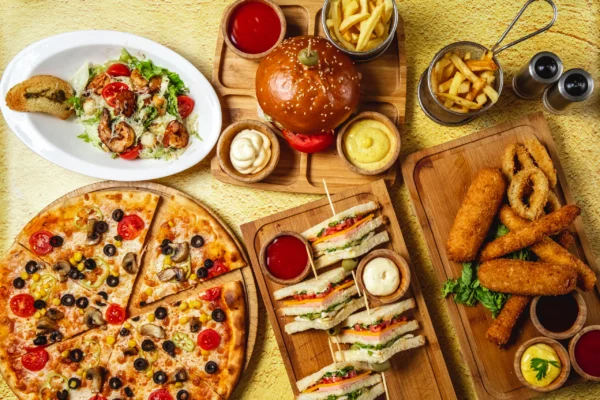 top-view-fast-food-mix-mozzarella-sticks-club-sandwich-hamburger-mushroom-pizza-caesar-shrimp-salad-french-fries-ketchup-mayo-cheese-sauces-table-scaled (1)